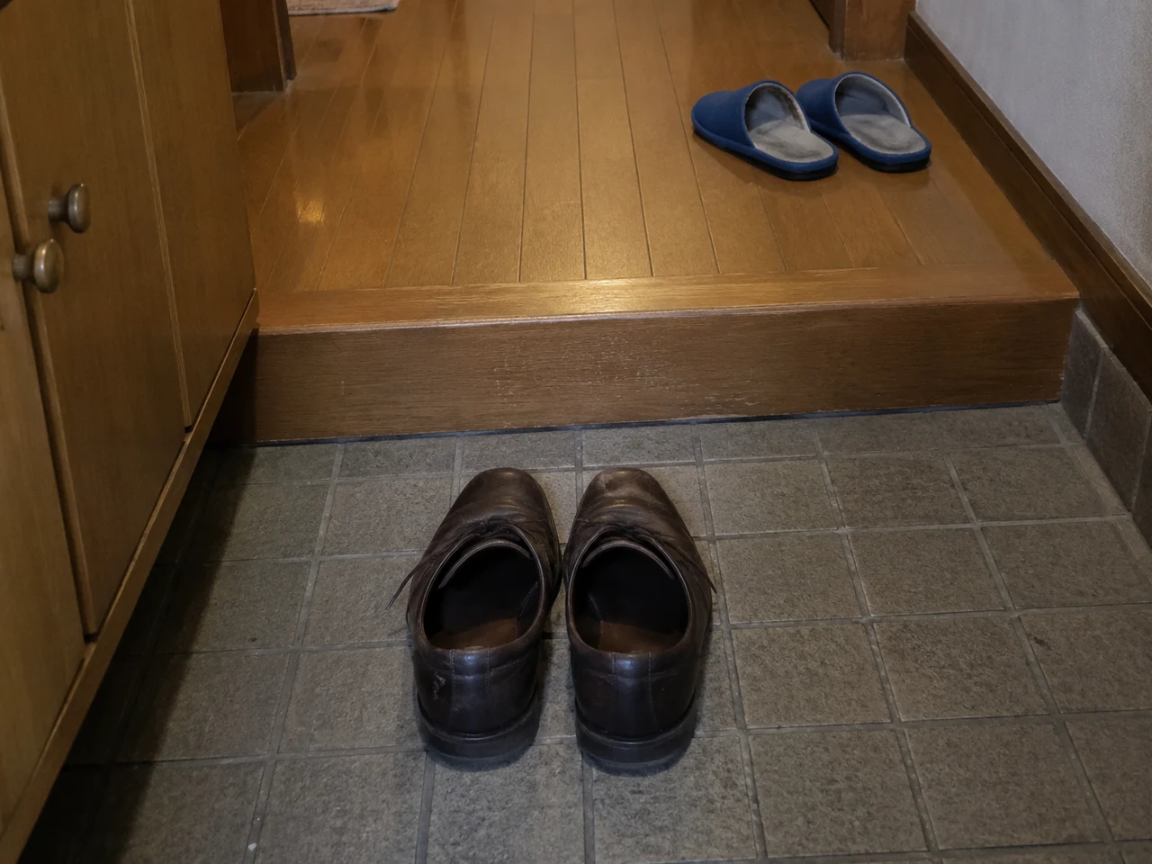 住宅の玄関。茶色の革靴一足が室内に向けてそろえられ、上がり框の奥に青いスリッパがある。