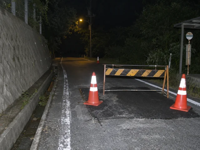 夜間の細い道路に置かれた規制用のバリケードとカラーコーン。街灯の先には人も車も見えない。